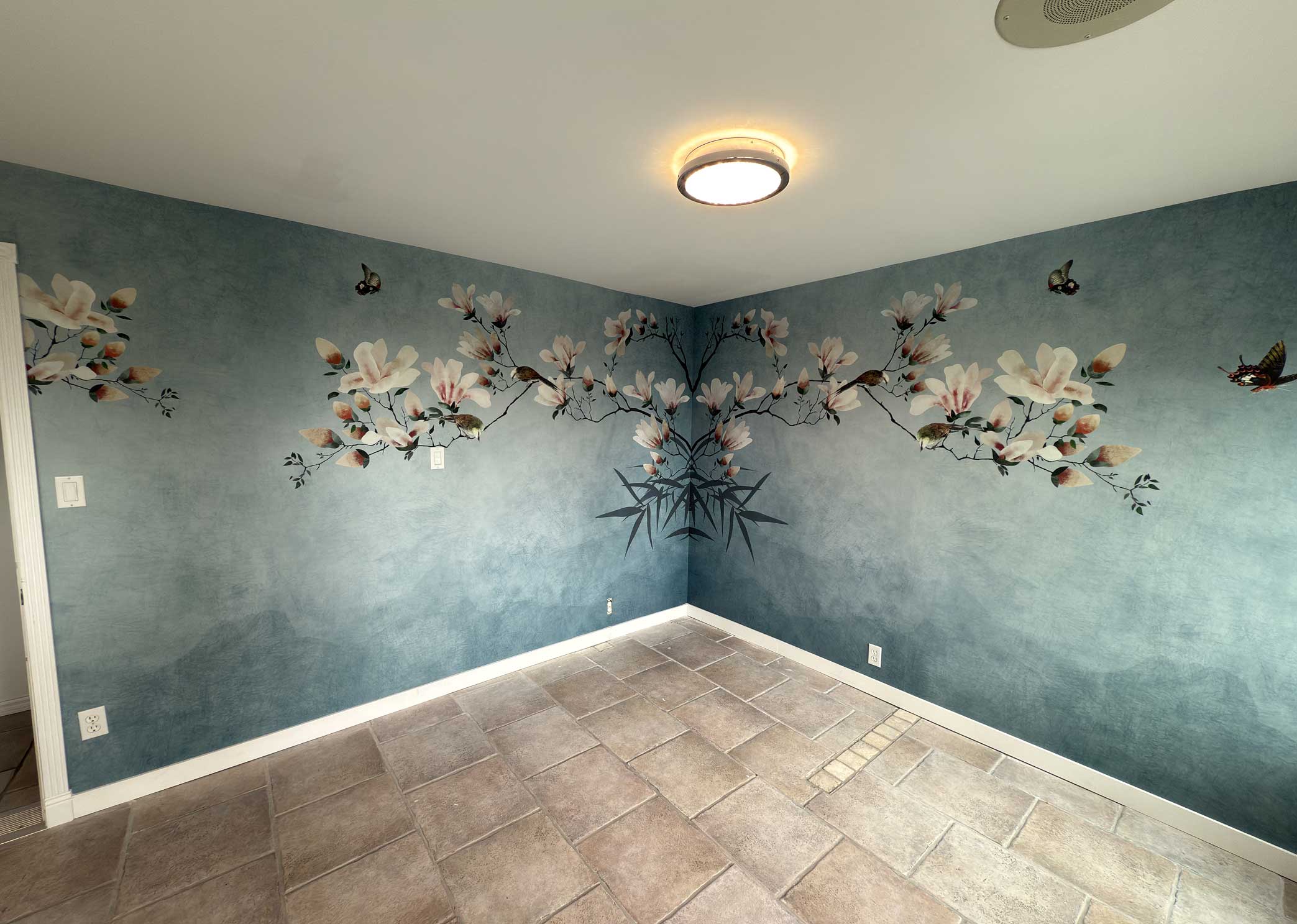magnolia-wallpaper-mural-corner-installation Blue magnolia and bird wallpaper mural installed across two walls, with the branch pattern mirrored and matched at the corner