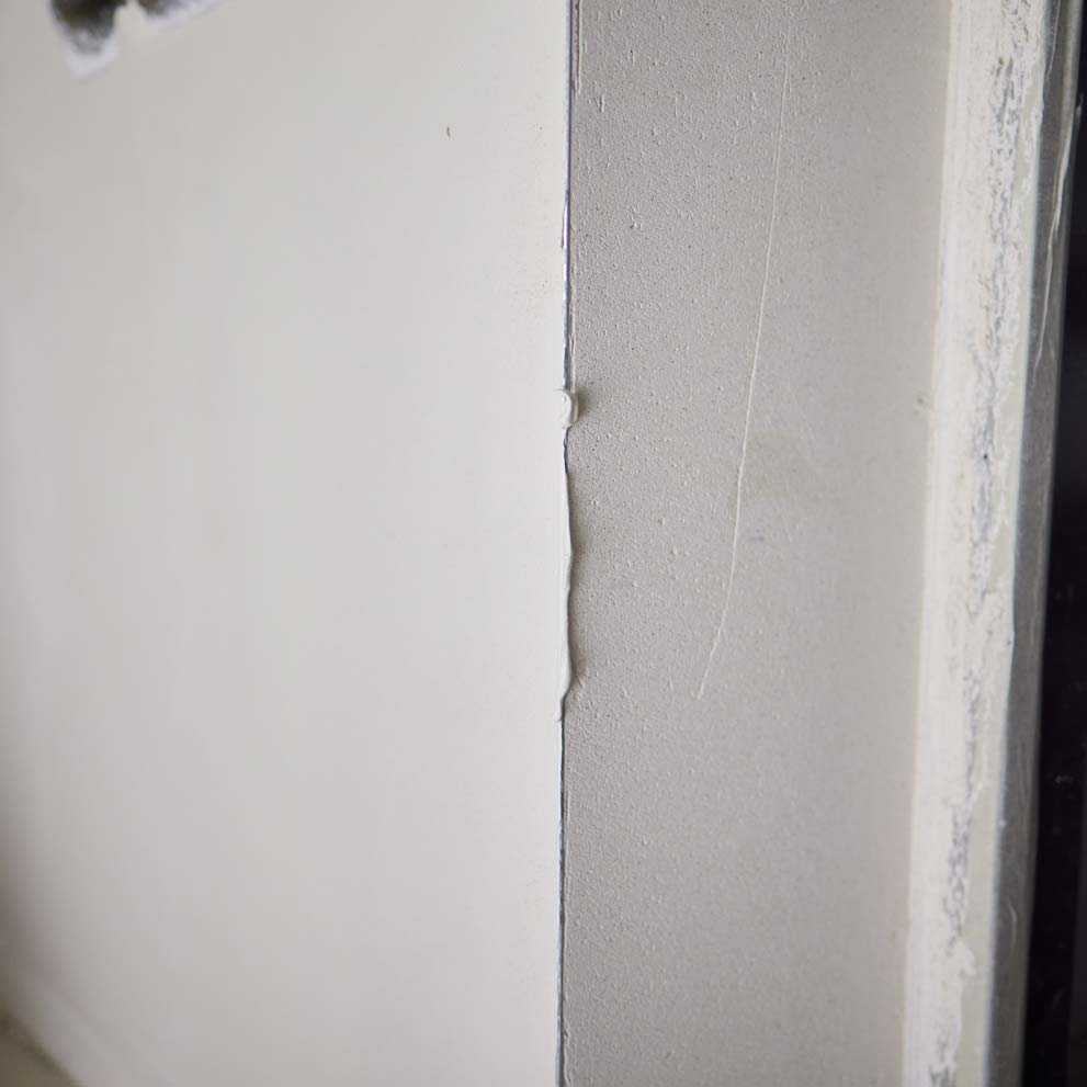 Close-up of a wall corner with a messy caulk blob, uneven paint line, and scuffed edge where two surfaces meet